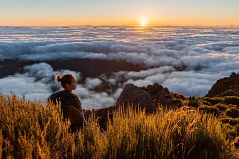 Woman sitting on a mountain watching the sunset over a sea of clouds, Pico Ruivo, Madeira,