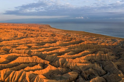 Landscape of eroded hills, badlands at sunset, Lake Issyk Kul in the background, aerial view,