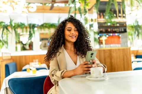 Beauty latin woman using mobile phone sitting on a cafeteria drinking coffee alone