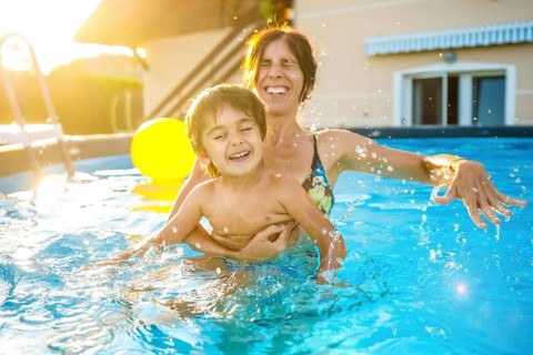 Mother and son are playing and laughing together in a home swimming pool during a sunny summer