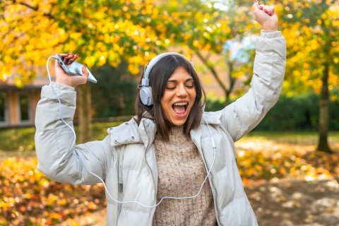 Happy vital caucasian young woman dancing listening to music in a park with fallen leaves in a