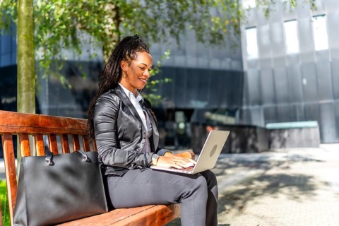 Hispanic elegant businesswoman sitting on city bench working with laptop in the financial district