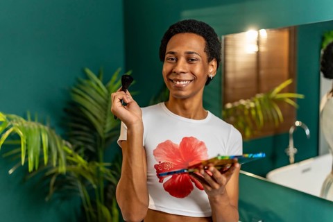 Happy latin young cute gay man holding a makeup palette smiling at camera in the bathroom