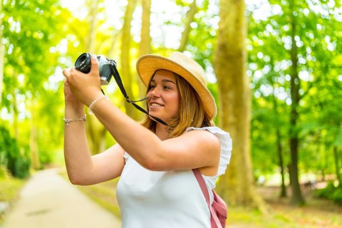Young female photographer making photos in nature standing in the middle of footpath among green