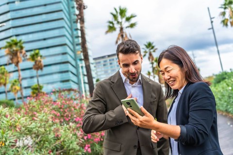 Multi-ethnic business coworkers using phone and smiling standing in a tropical modern city