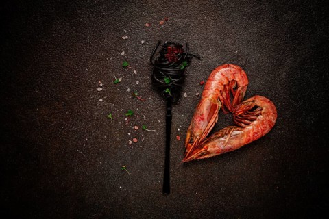 Black spaghetti, wrapped on a fork, langoustines in the shape of a heart, on the table, dish