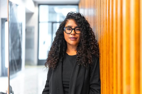 Portrait of a relaxed latin young businesswoman standing and leaning in an office corridor