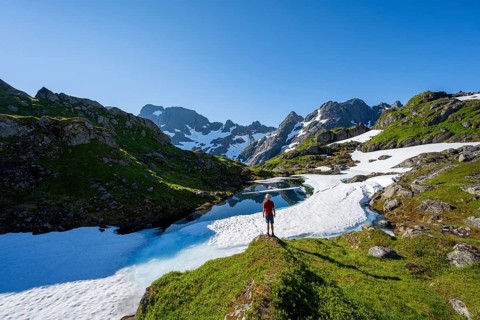 Mountaineer in front of lake with snow remains, Landscape at the mountain hut Trollfjord Hytta,