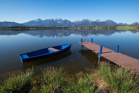 A jetty with a blue boat on a quiet lake with an impressive mountain view, Hopfen am See, near