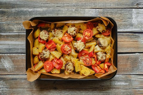 Overhead view of roasted potatoes, mushrooms and tomatoes garnished with melted cheese, arranged in