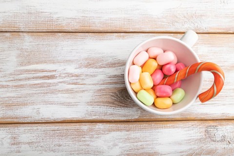 Heap of multicolored caramel candies in cup on white wooden background. copy space, top view, flat
