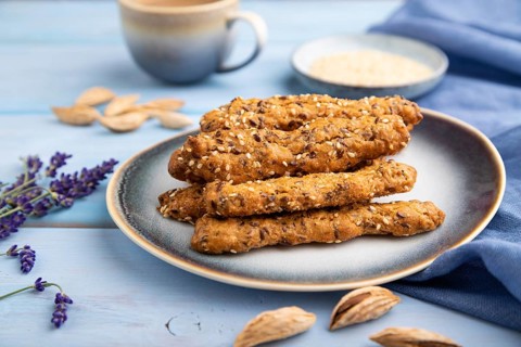 Crumble cookies with seasme and almonds on ceramic plate with cup of coffee and blue linen textile