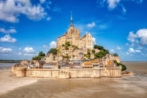 Majestic abbey on a mountain in a vast landscape under a partly cloudy sky, Le Mont-Saint-Michel