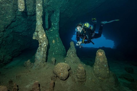 Scuba diver female diver swimming dives in entrance area of underwater cave stalactite cave