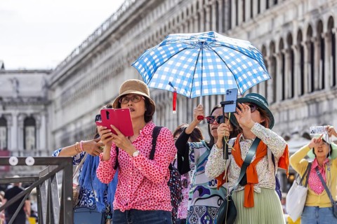 Tourists from Asia with mobile phones and parasols taking photos. Souvenir photo of St Mark's