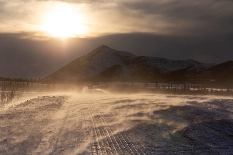 Snow-covered gravel road in the wind in front of mountains, backlight, ice, Dalton Highway, Alaska,