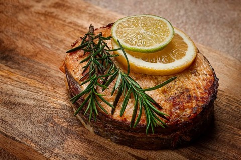 Salmon steak, fried, on a cutting board, top view, rosemary, lemon and lime, homemade, one serving,