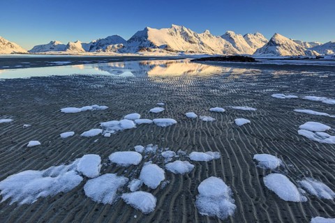 Ice floes on the beach in front of snowy mountains, evening light, winter, Moskenesoya, Lofoten,