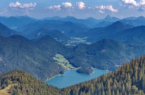 A wide panorama of mountains and valleys with extensive forests under a blue sky with clouds,