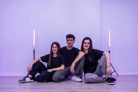 Three young dancers are sitting together on the floor of their dance studio, taking a break and