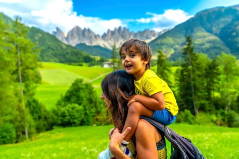 Mother carrying her son on her shoulders while enjoying the view of the odle mountains and the