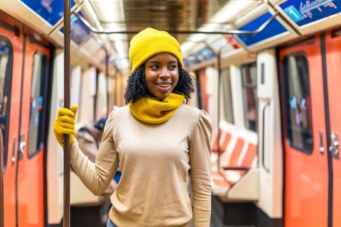 Young black woman wearing yellow wool cap and gloves standing inside subway train, holding handrail
