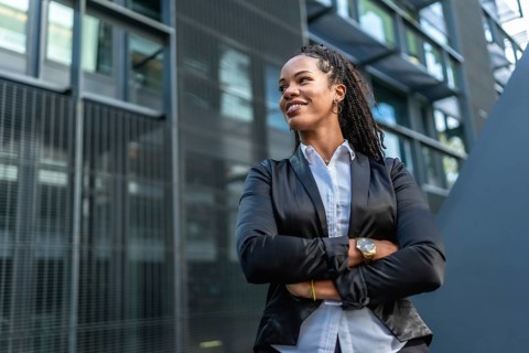 Female Latin entrepreneur smiling proud standing with arms crossed outside a block office