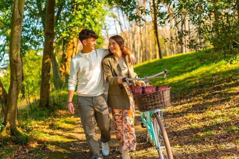 Happy young couple walking through a sunlit forest path with a vintage bicycle, embracing the