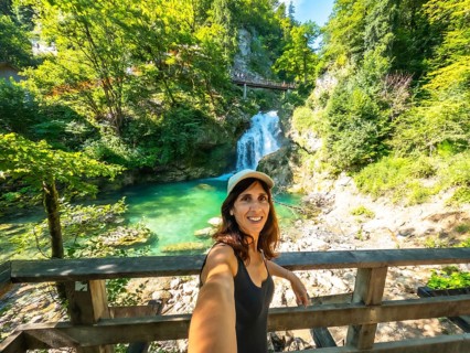 Woman taking selfie with waterfall and turquoise colored water of tolmin gorges in the background,