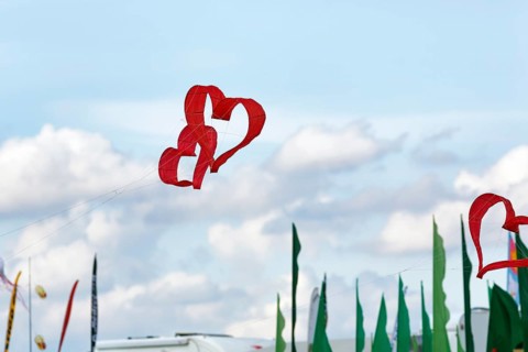 Two red heart-shaped kites flying intertwined in the sky, text free space, kite festival in