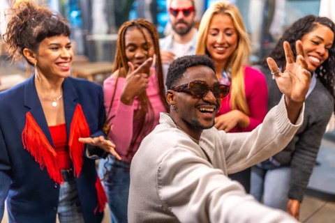 Multi-ethnic friends waving at camera taking selfie during a night party in a bar terrace