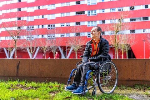 Young man sitting in wheelchair enjoying a sunny day in a modern urban park with a red building in