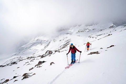 Two ski tourers in a wintry mountain landscape with cloudy mountain peaks, ascent to Piz Laviner,