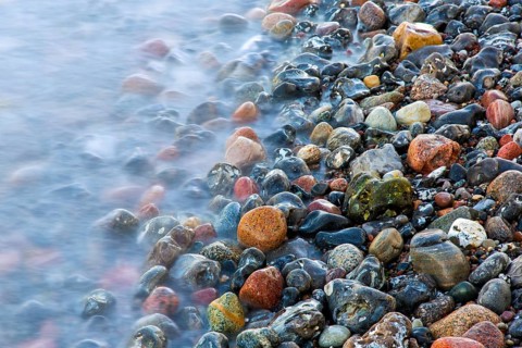 Blurred sea water of wave rolling over wet colourful pebbles on shingle beach, cobble beach