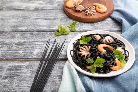 Black cuttlefish ink pasta with shrimps or prawns and small octopuses on gray wooden background and