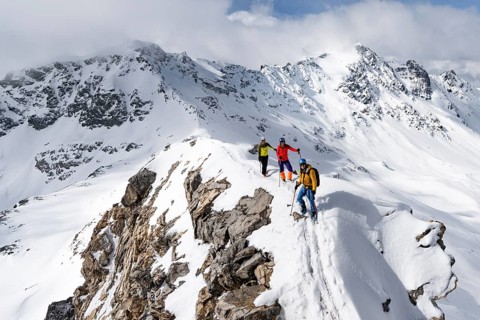 Three mountaineers climbing the narrow ridge of Piz Laviner, view of mountain panorama in winter
