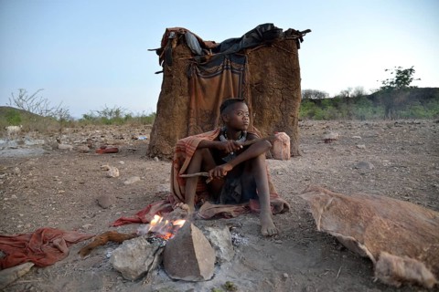 Young shepherdess from the Himba people sitting at a campfire in front of her hut, Ombombo,