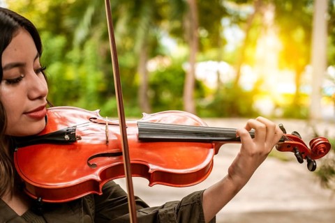 Close up of a girl with her violin playing a melody outdoors, Concept of smiling female violinist.