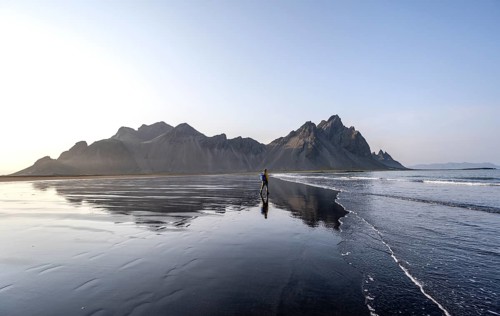 Tourist at black lava beach, sandy beach and sea, mountains Klifatindur reflected in the water,