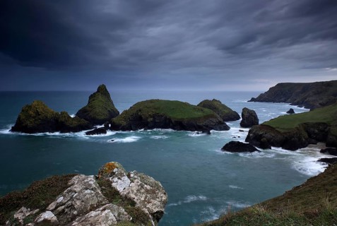Dramatic clouds on rocky coast, rising rain shower over rocky islands with foaming surf, Kynance