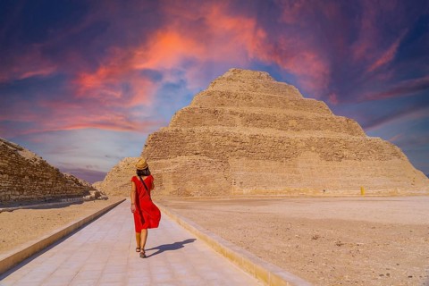 A young tourist in a red dress at the Stepped Pyramid of Djoser at sunset, Saqqara. Egypt. The most