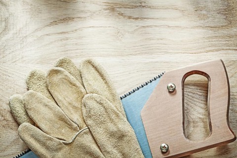 Pair of leather protective gloves sharp hacksaw on wooden board construction concept