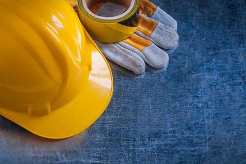Safety tape yellow building helmet and protective gloves on scratched vintage metallic background