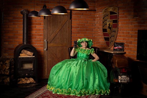 Woman in green dress sitting in a rustic room with fireplace and wood panelling, Staged photo