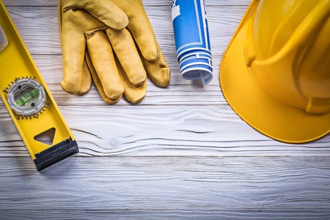 Assortment of working gloves hard hat blue rolled blueprints construction level on wooden board