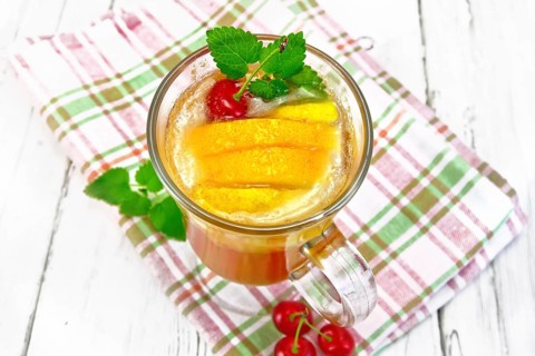 Lemonade in a wineglass with cherry, lemon and orange, mint on a napkin on a wooden plank