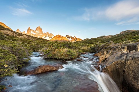 A waterfall with the Fitz Roy mountain illuminated by the morning sun in the Los Glaciares National