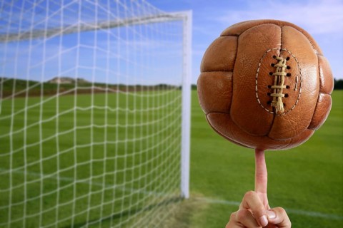 Football vintage ball in hand net soccer goal green grass background