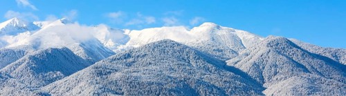 Winter travel vacation nature panoramic background with snow covered mountain peaks and blue sky