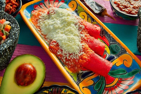 Red enchiladas Mexican food with guacamole and sauces on colorful table
